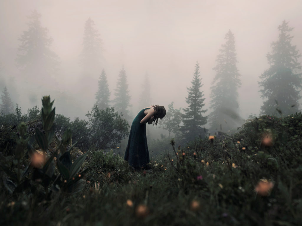 Emotional self portrait showing a woman who appears to be crying in a foggy forest landscape.