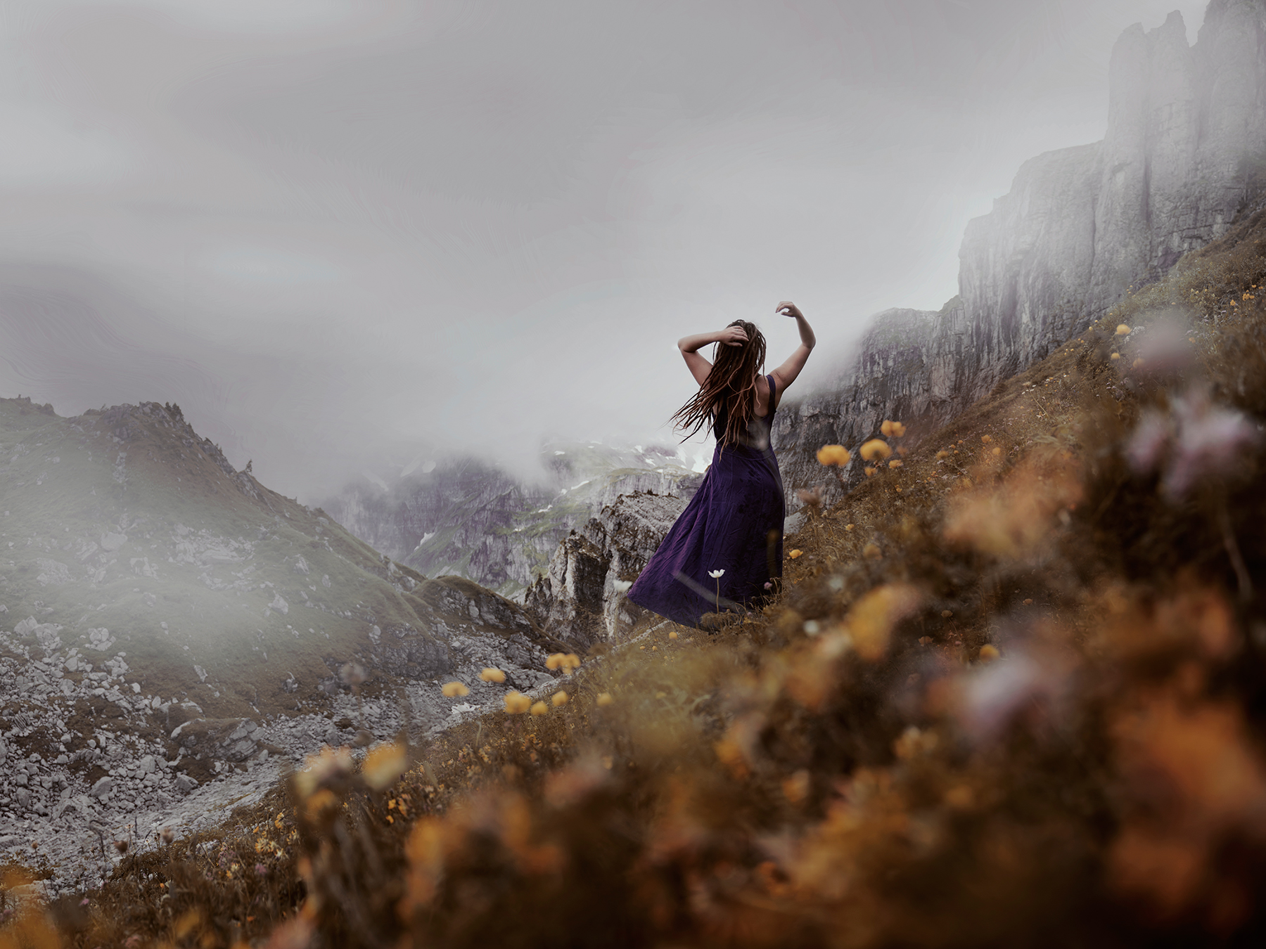 Artistic self portrait of a woman standing in a beautiful mountain landscape in a dress, wind flowing through her hair.