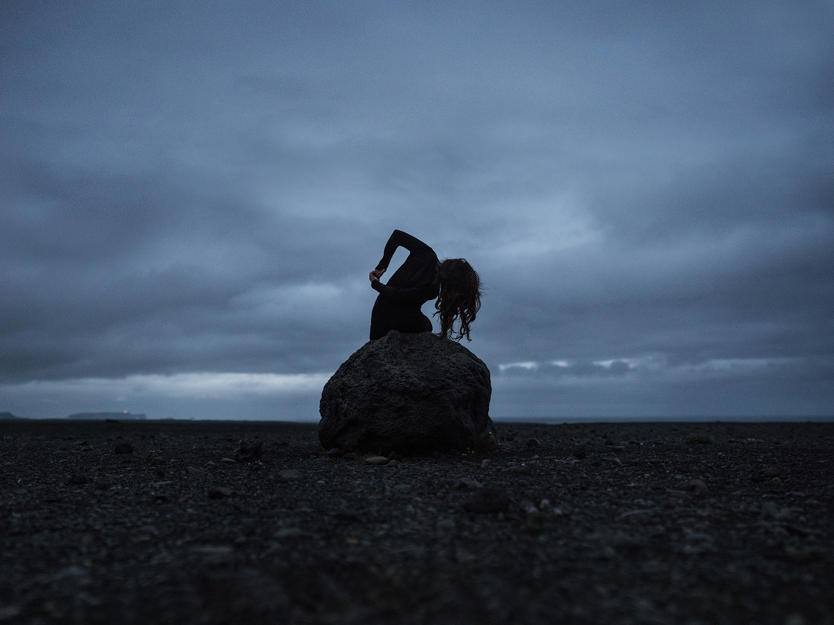 Self portrait photography showing a dark figure on a rock under a cloudy sky in Iceland.