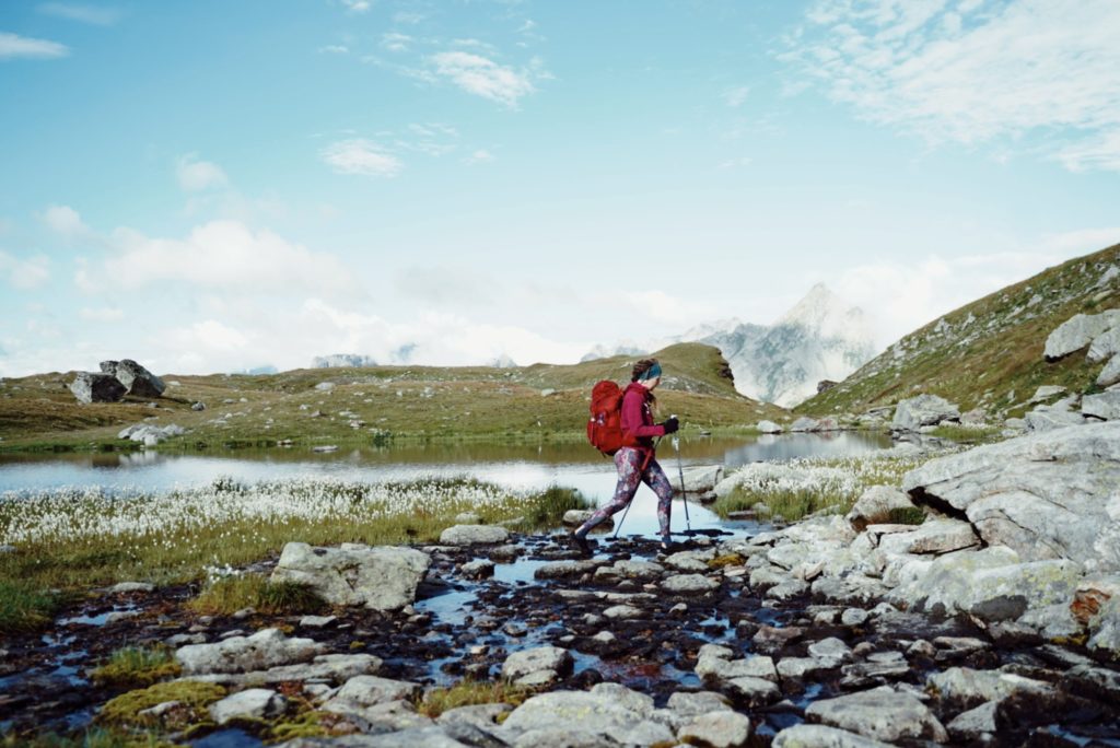 A female backpacker crossing a mountain stream holding trekking poles.