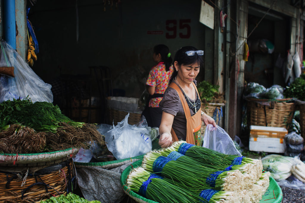 A market woman in Bangkok, Thailand, reaching for a pile of spring onions.