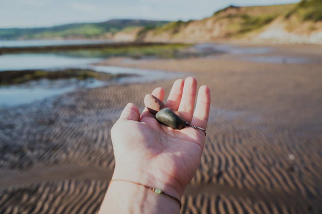 A hand holding two stones at a beach