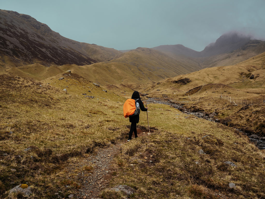 A long distance hiker with an orange rain cover hiking through a rainy landscape.