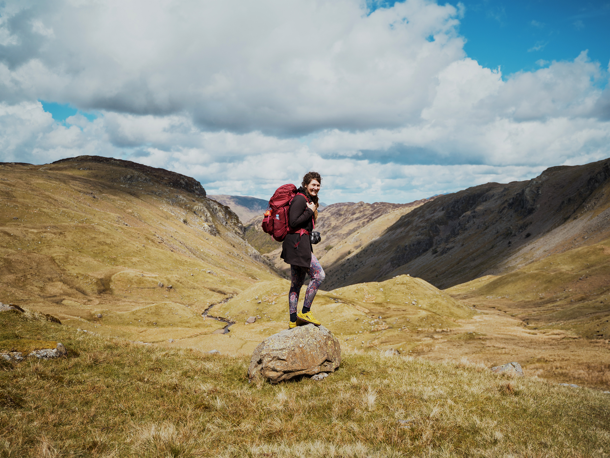 A female solo hiker standing on a rock in a mountain landscape along Wainwright's Coast to Coast Way.