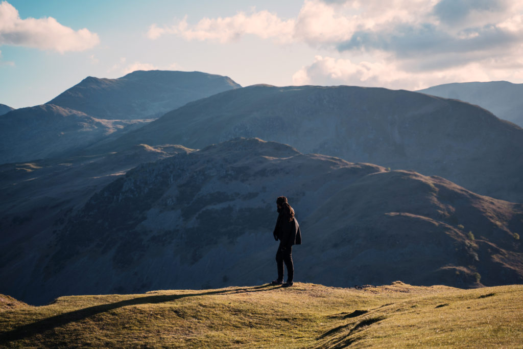 A man standing in the Lake District mountains with an epic view at sunset