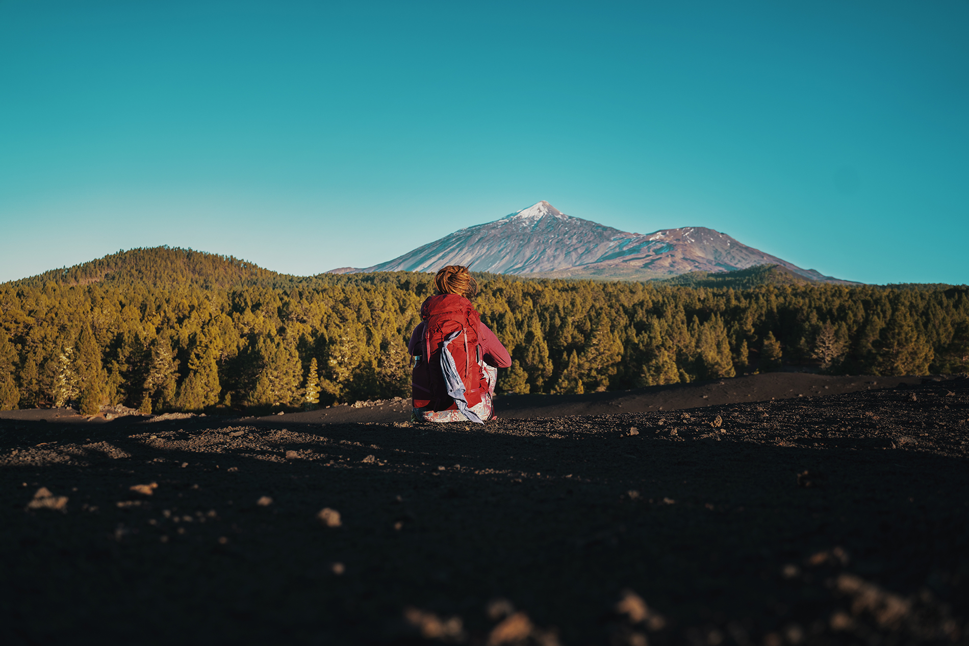 A backpacker resting in front of a volcanic mountain landscape.
