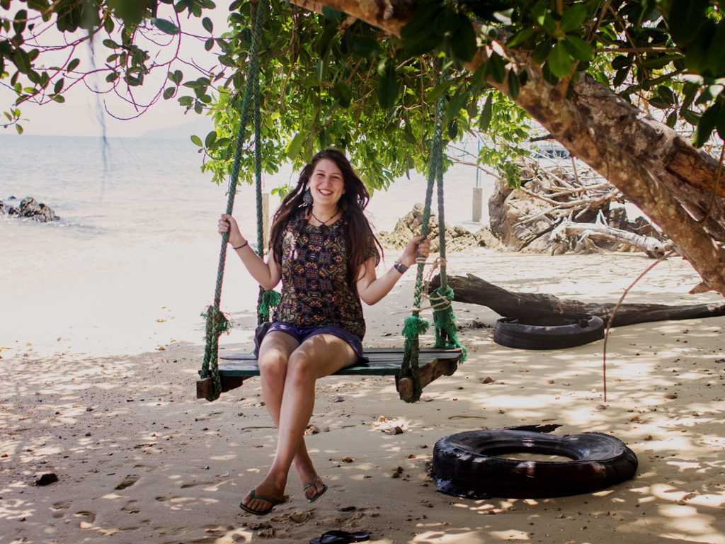 A young, smiling woman on a swing by the beach in Thailand.