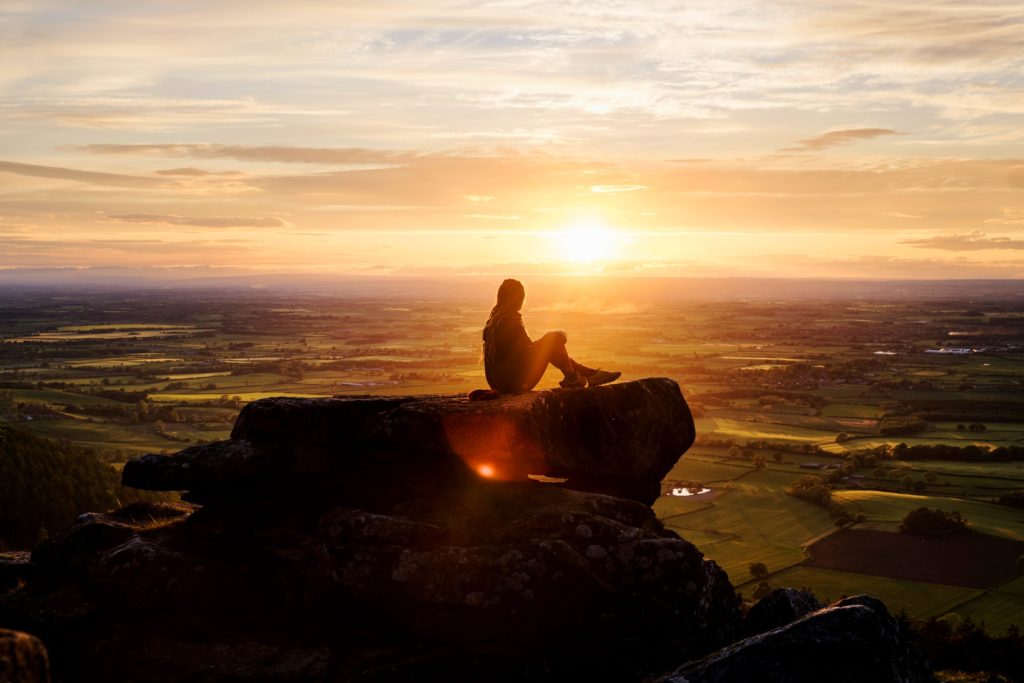 A hiker sitting high above a flat landscape watching the sunset.