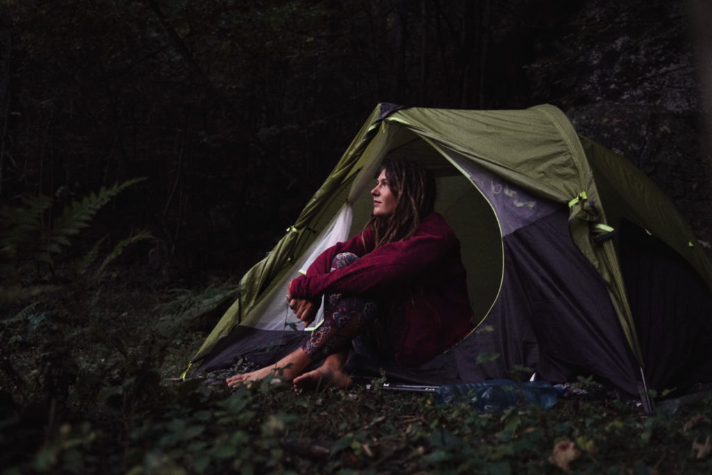A woman sitting alone in front of her tent camping in the dark.