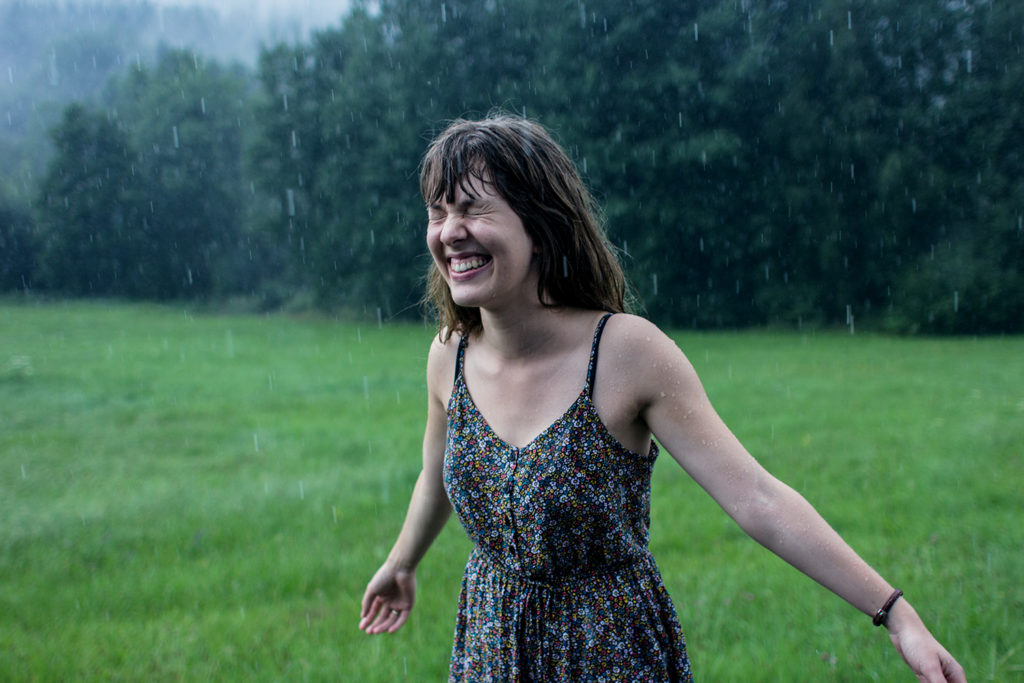 A young woman dances in the rain and laughs joyfully.
