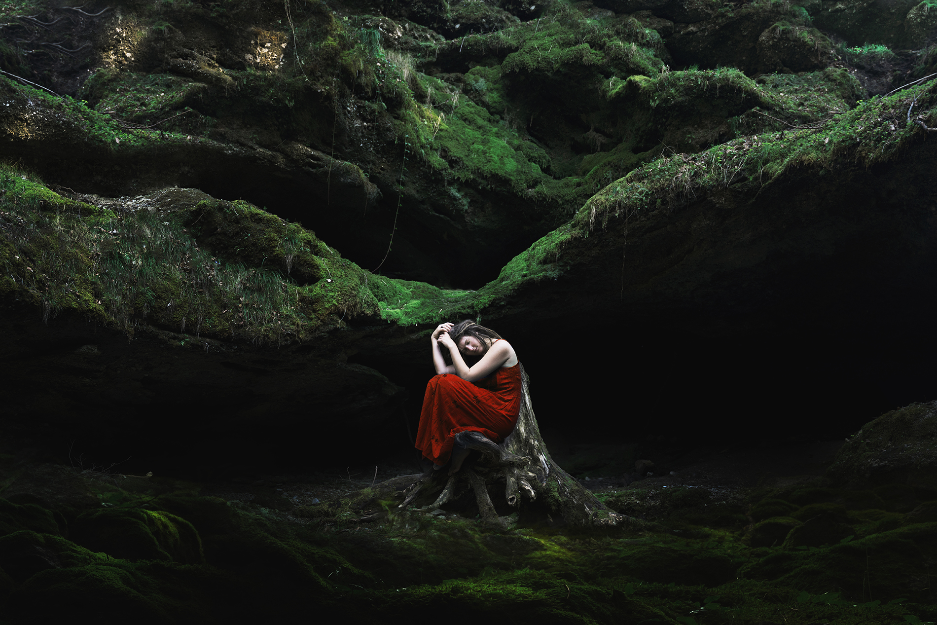 An artistic self portrait showing a woman in a mossy forest in a pensative pose and dealing with discomfort.