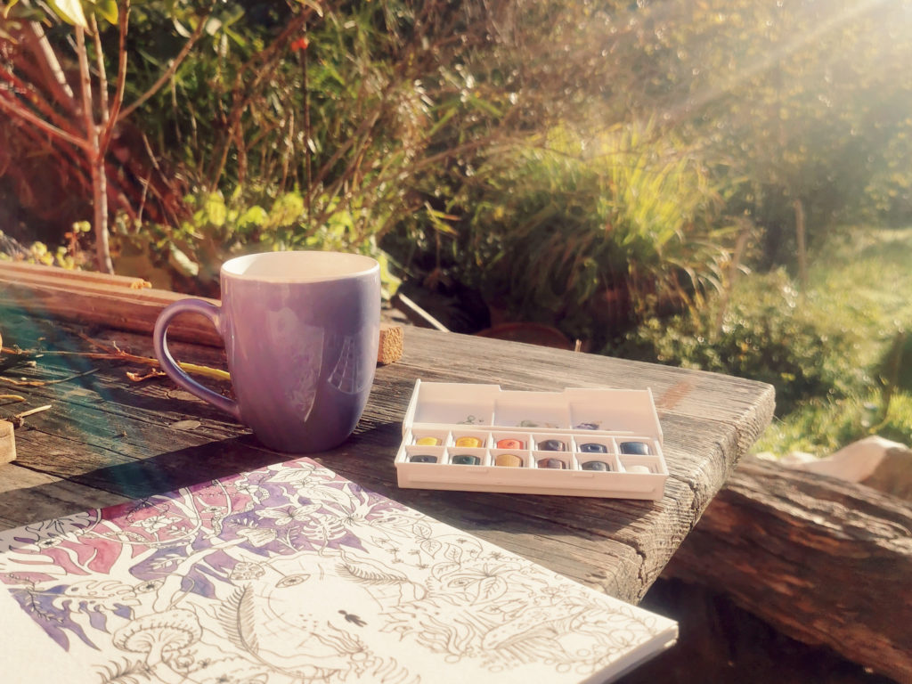 A watercolor painting and a cup of coffee on a table in the sunny garden - a creative artist date idea.