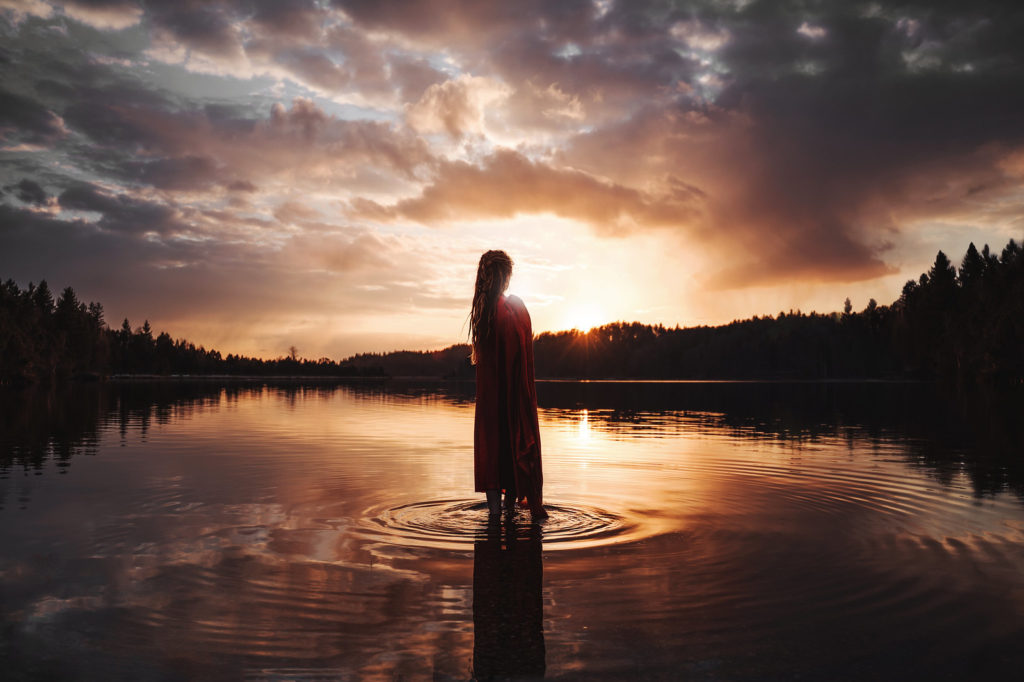 A creative photo of a woman standing in a lake at sunset.