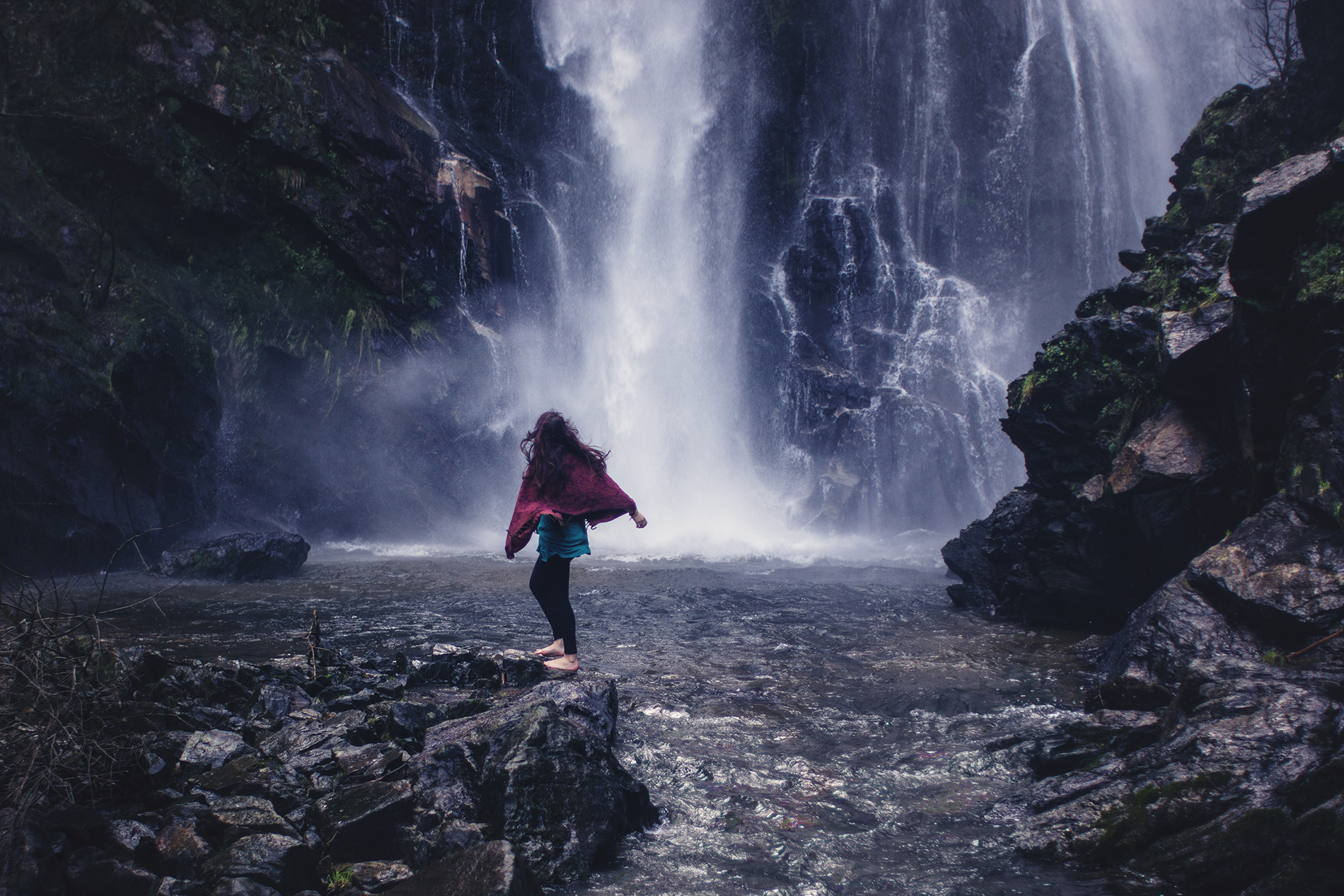 A young woman who travels for free dancing happily under a waterfall.