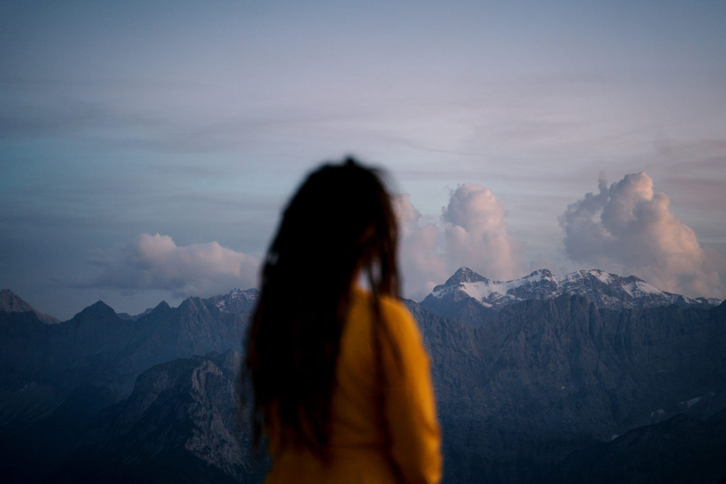 Traveling mindfully and slow travel means to take in the moment and enjoy. The picture shows a girl looking at the mountains far away, a dreamy moment.