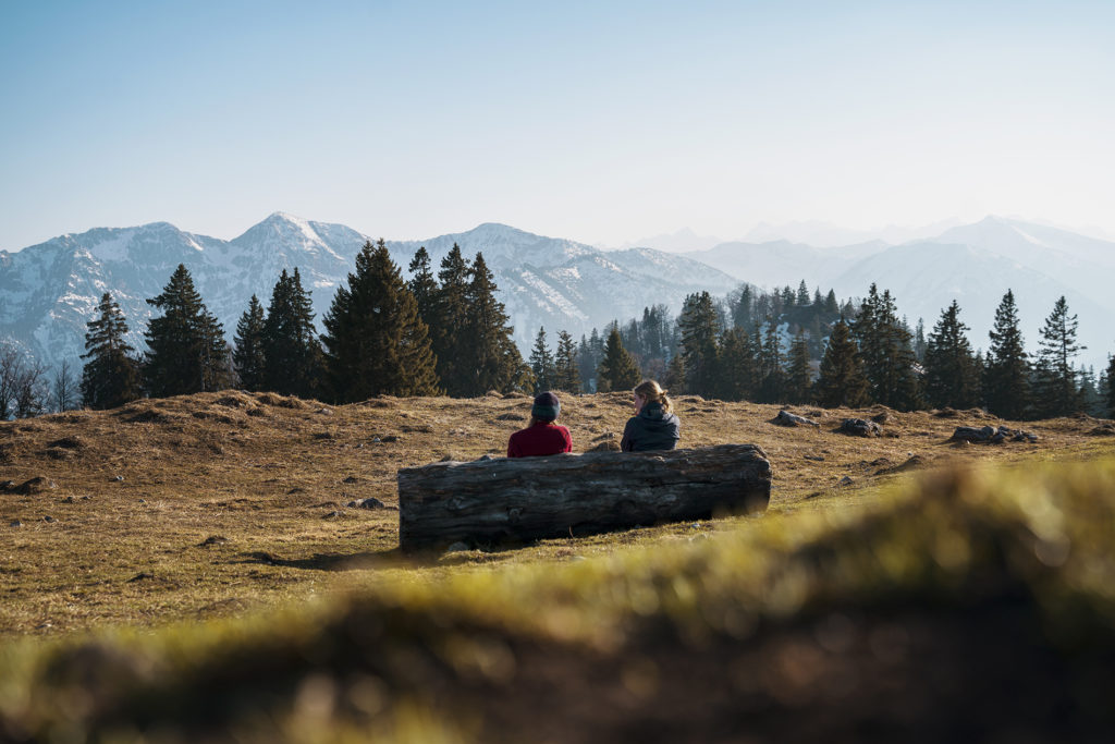 One important life change can be to get outdoors more - in this image, two people sit on a bench, surrounded be a beautiful view of the Alps in the sunshine.