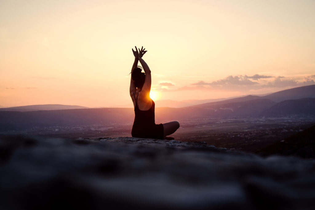 A woman lifting her arms above her head in the sunset, enjoying the moment.