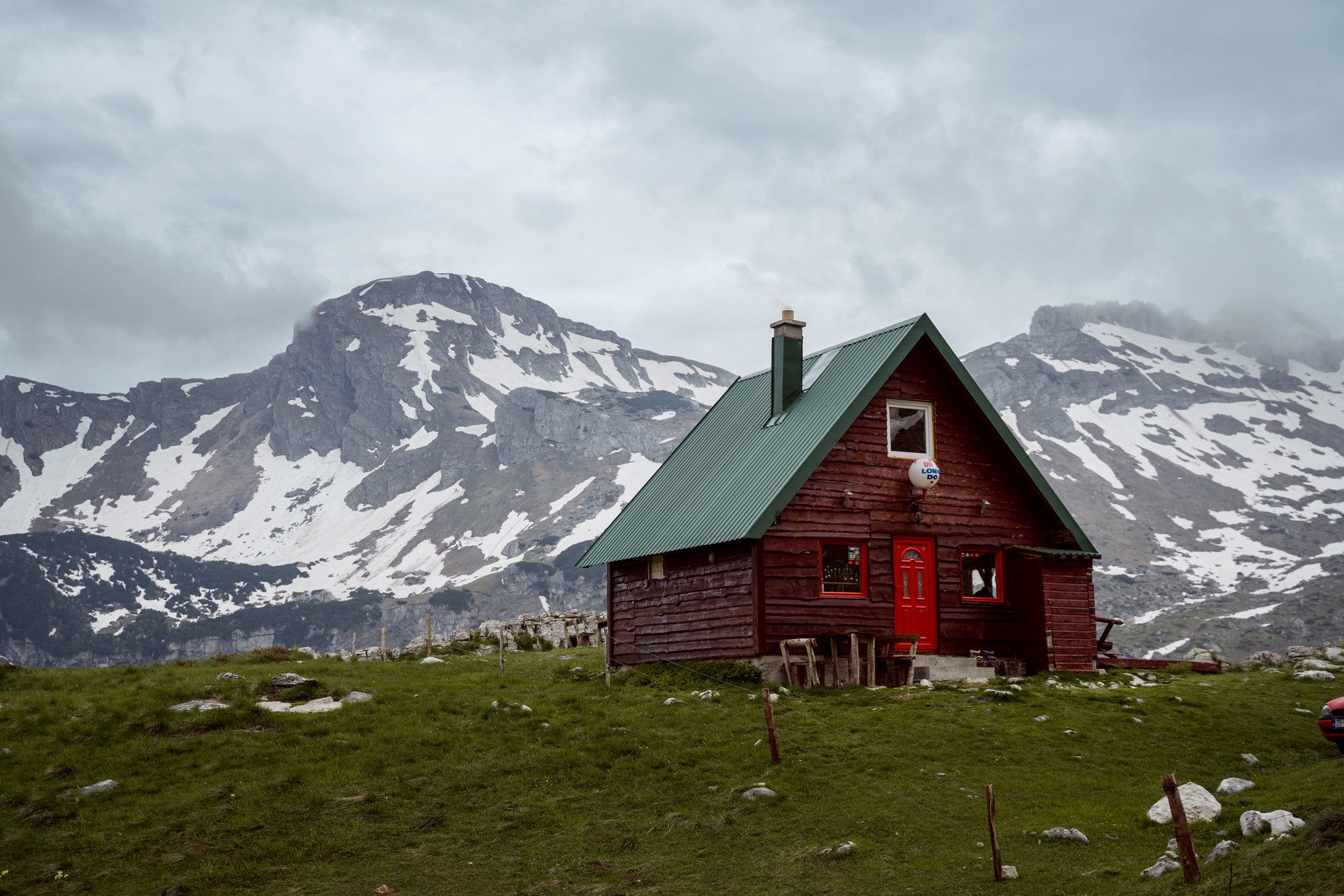 A mountain hut in Montenegro in front of snow-covered peaks.