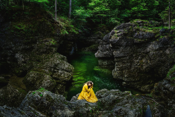 Tranquil, artistic self portrait photography in nature. The depicted woman wears a yellow dress which creates a beautiful contrast with the green environment of a gorge.