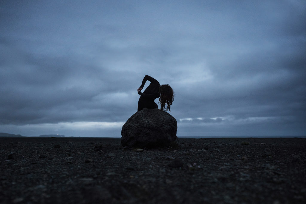 Dark, moody Fine Art Photograph taken in Iceland. A woman on a rock in a desolte landscape. Title: "Dance of the Insomniac" by Anna Heimkreiter