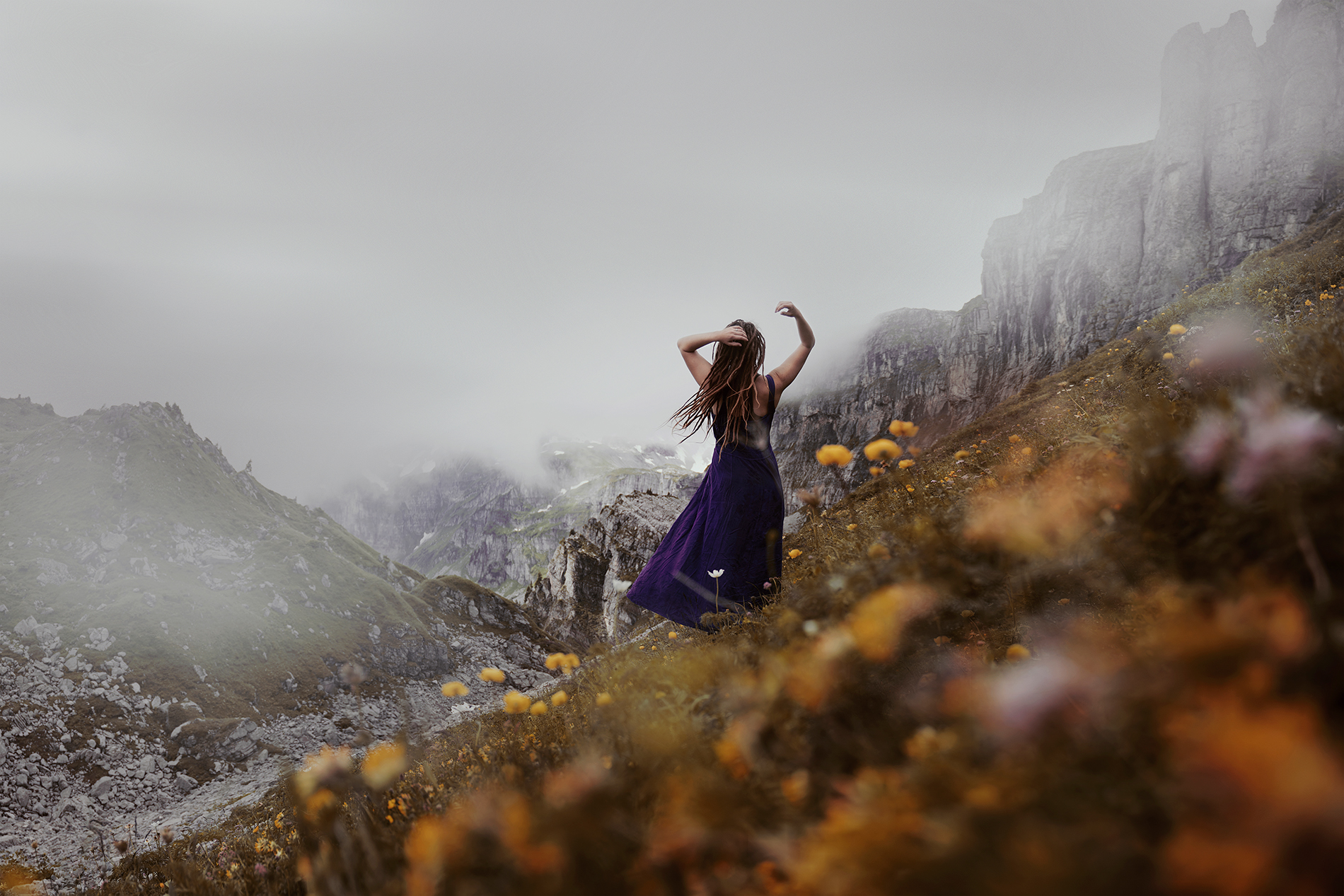 Artistic self portrait photography is a way of creative expression. This self-portrait by Anna Heimkreiter features a woman in a long dress standing in a beautiful mountain scenery. Her dress and hair flow with the wind, creating an ethereal atmosphere.