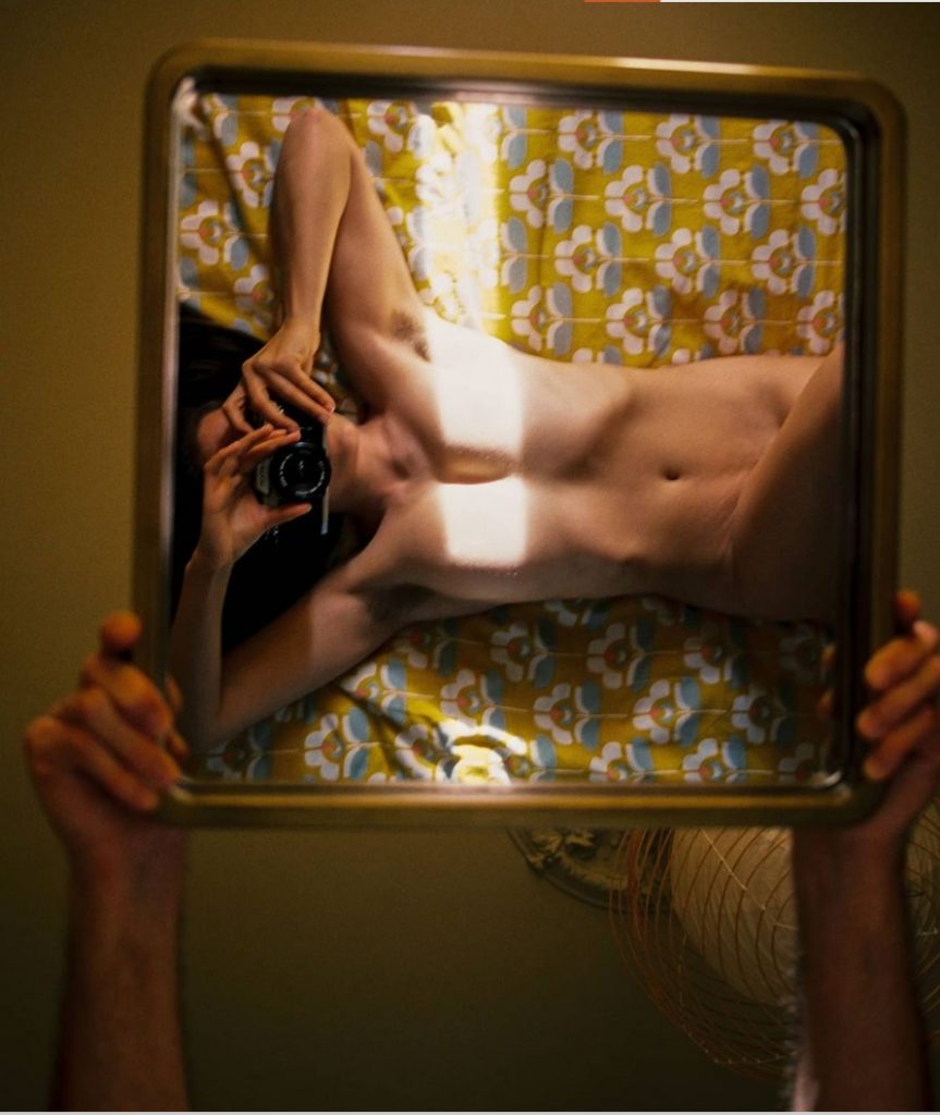 Creative nude self-portrait in a mirror held above the artist.