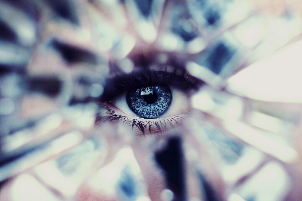 Mirror self-portrait photography by Anna Heimkreiter. A piercing blue eye surrounded by broken mirror pieces.