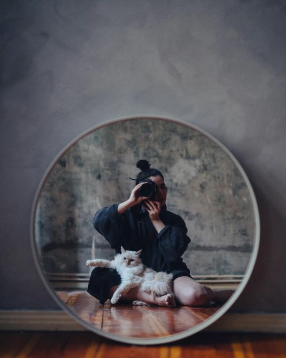 A woman photographs herself and her cat in a mirror.
