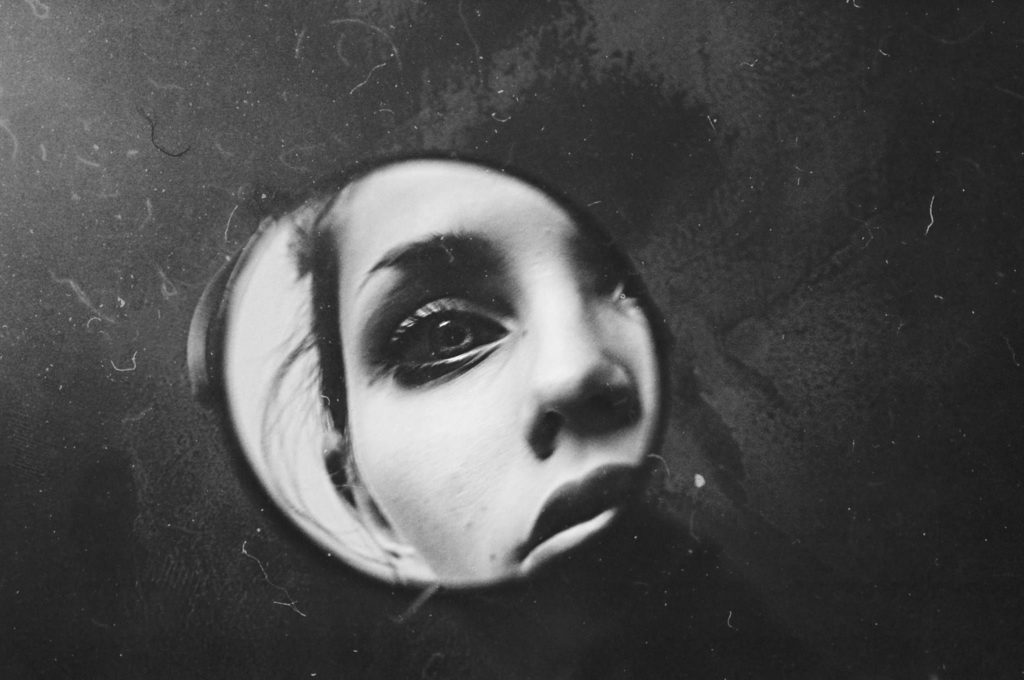 Black-and-white self portrait in a small mirror showing the face of a young woman.